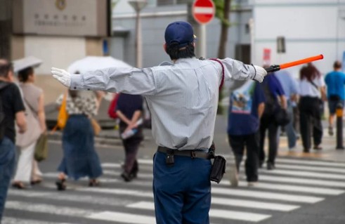 横断歩道で両腕を広げ歩行者を誘導する警備員